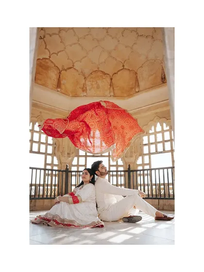 A creative shot using a vibrant red Bandhani dupatta to create a dramatic canopy. This photo, taken inside a heritage location, showcases our ability to blend cultural elements with artistic composition.