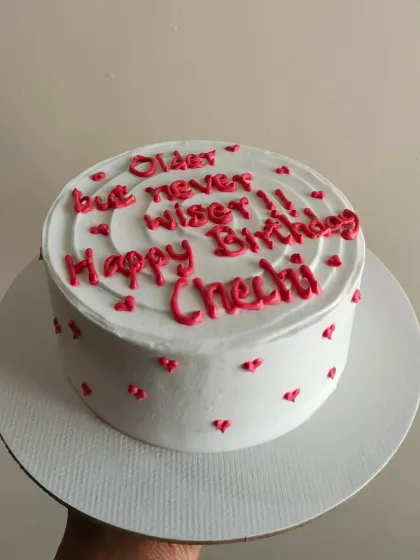 A cheeky "Older but never wiser" message on a minimalist cake with tiny hearts.