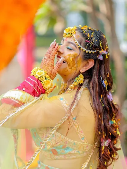 A candid moment of the bride laughing, with turmeric paste on her face and flowers in her hair. This photo embodies the playful and heartfelt nature of the Haldi ritual.