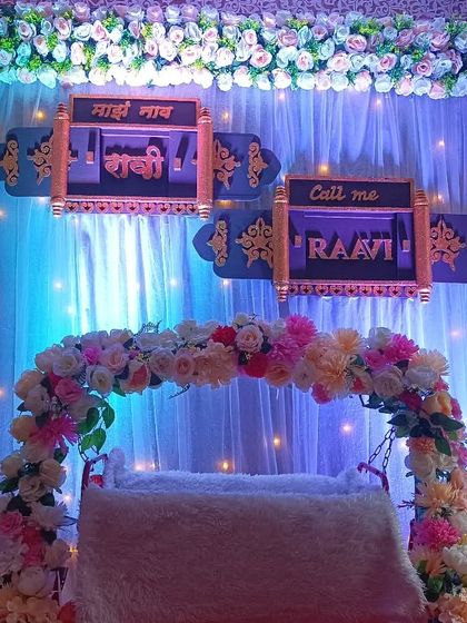 An elegant floral decoration for a naming ceremony. The setup includes a decorated cradle, a fairy light curtain, and custom signs revealing the baby's name in Marathi and English.