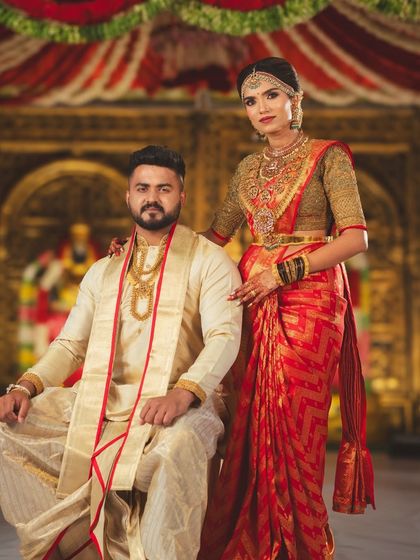 A royal portrait of the couple seated at their wedding ceremony. The decor is inspired by temple architecture, with ornate golden backdrops and traditional attire.