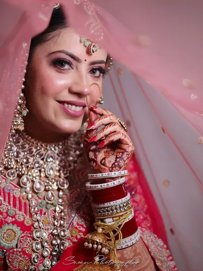 A beautiful close-up of the bride smiling from behind her veil, highlighting her intricate nath and henna.