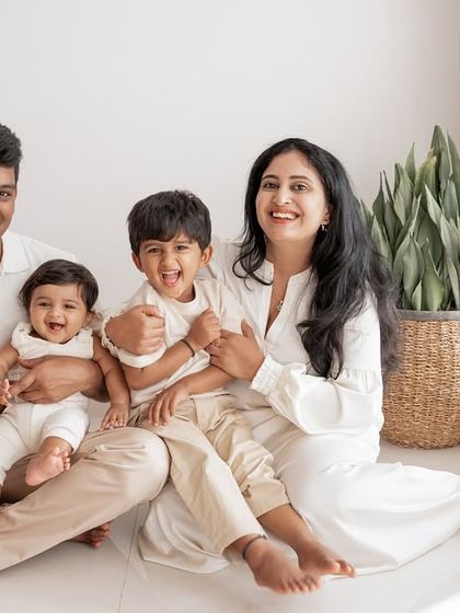 A happy family of four, all dressed in neutral tones, sitting together for a classic portrait.