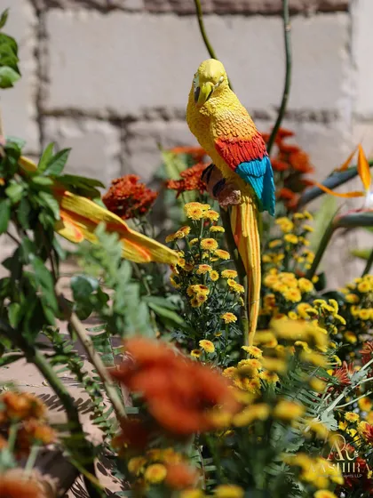A whimsical detail of a colorful parrot figurine perched among bright yellow and orange marigolds.