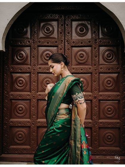 Elegance is timeless. A beautiful profile shot of the bride in her green silk saree, standing before a traditional carved wooden door.