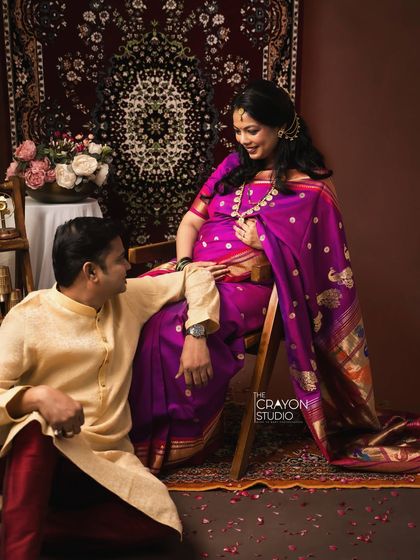 He looks at her with adoration as she smiles, seated gracefully. This pose captures the dynamic of their relationship and their shared excitement.