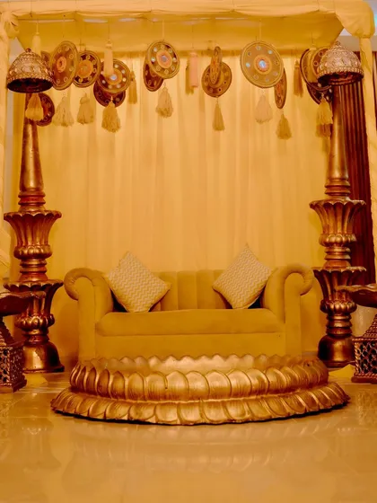 The Haldi setup at the groom's place, featuring a golden lotus-themed sofa and traditional pillar props.