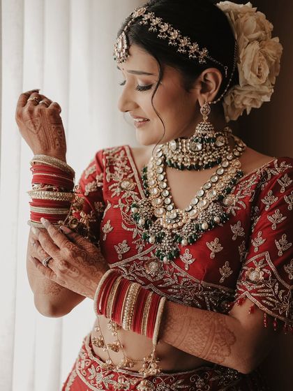 A classic getting-ready shot. The bride adjusts her bangles by the window, the soft natural light beautifully illuminating her intricate jewelry and happy expression.