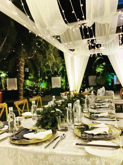 An intimate outdoor sit-down dinner setup with a canopy of white drapes and fairy lights. This creates a romantic, starlit dining experience.