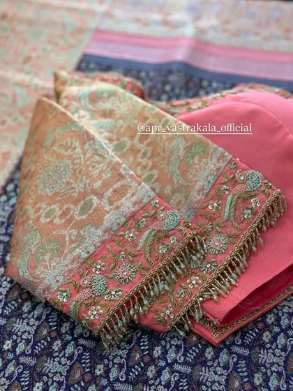 The sleeve of a peach-colored blouse, featuring intricate bird motifs embroidered in pastel threads and finished with a beaded tassel border.
