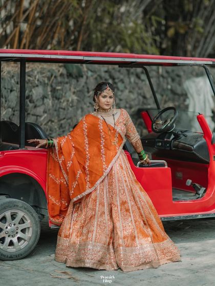 The bride poses with a vibrant red buggy, her orange lehenga creating a stunning color contrast. A fun and stylish bridal portrait.