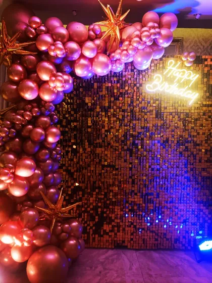 For a touch of glam, nothing beats a shimmer wall. This stunning rose gold sequin backdrop is paired with a matching balloon garland and a 'Happy Birthday' neon sign, creating the perfect photo-op spot for teens and adults. It's all about that Insta-worthy effect!
