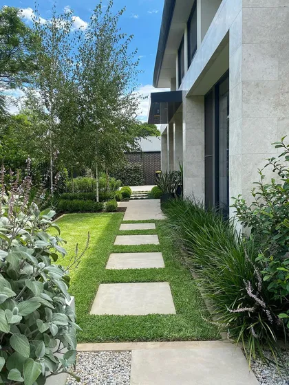 A well-designed garden path does more than connect spaces; it creates a journey. Here, I used clean, modern pavers set in a perfectly trimmed lawn, flanked by soft, layered plantings to create an elegant and inviting walkway alongside a contemporary home.