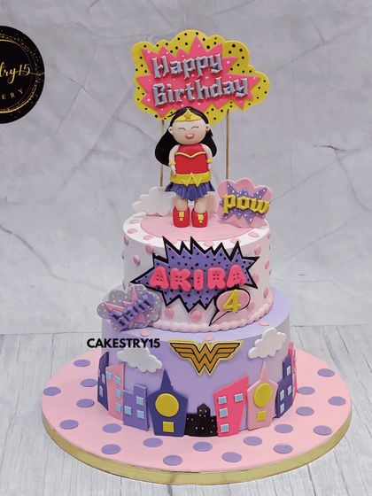 A heroic Wonder Woman-themed cake for a fourth birthday. This two-tier chocolate cake features the iconic superhero, a city skyline, and comic book-style bursts, perfect for a little superheroine.