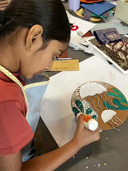 A student meticulously glues down textured materials to create her collagraph plate, which will be used to make an intaglio print.
