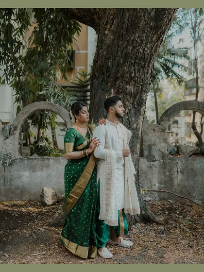 Showcasing classic Marathi elegance, this couple's portrait is set against a rustic tree and stone wall. Her deep green Nauvari saree and his white kurta create a timeless look, perfect for heritage-themed engagement photos.