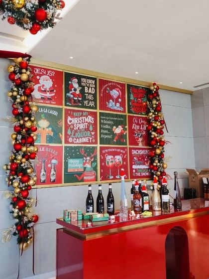 A festive bar setup with a custom backdrop of vintage-style Christmas posters and garlands of red and gold ornaments.