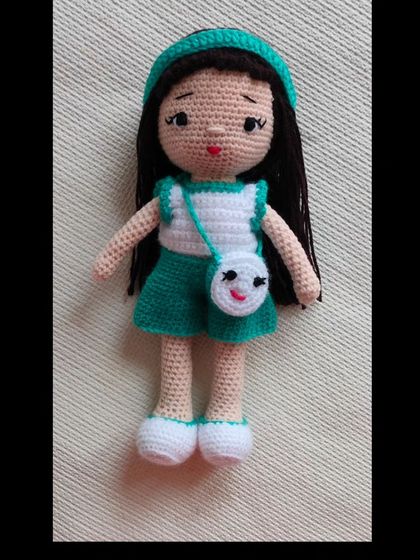 A cute doll in a green and white outfit with a smiley face bag. Her headband, dress, and shoes can all be removed for dress-up play.
