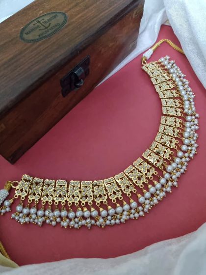 The 'कफ़ूरी' (Kafuri) necklace, a beautiful choker with intricate gold-plated work and pearl drops. This piece offers a classic, timeless look perfect for any celebration.