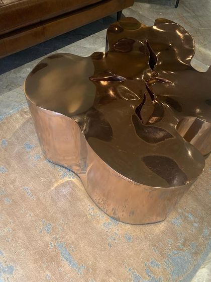 A sculptural, biomorphic coffee table in polished copper, reflecting the light and the colors of the room.