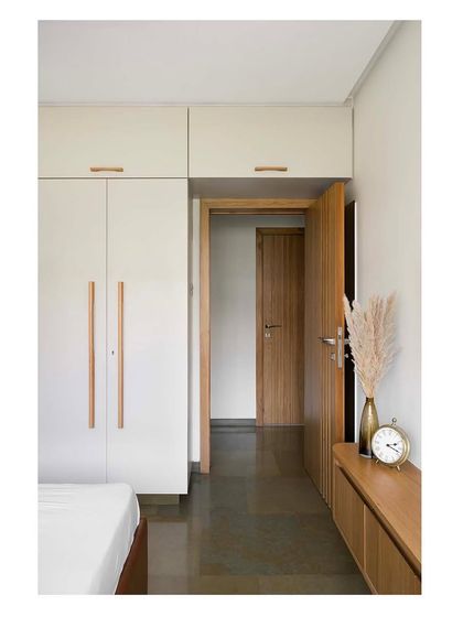 A minimalist bedroom in a Mumbai residence, featuring clean lines, floor-to-ceiling wardrobes with custom wood handles, and a calm, neutral palette to create a restful atmosphere.