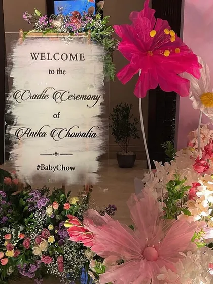 A personalized acrylic welcome sign for the cradle ceremony, surrounded by a lush arrangement of flowers. It's the first beautiful detail guests see.