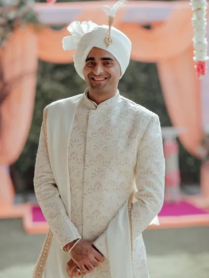 A simple, happy portrait of the groom in his elegant white sherwani, his smile full of warmth and anticipation for the ceremony.
