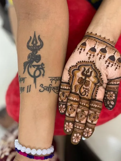 A powerful design for Sawan, combining a client's existing Trishul tattoo with a matching mehendi Trishul and 'Om' symbol on the palm.