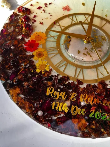 A close-up of a 12-inch clock with a mix of colorful preserved flowers. The bright yellow and red flowers really stand out against the darker rose petals.