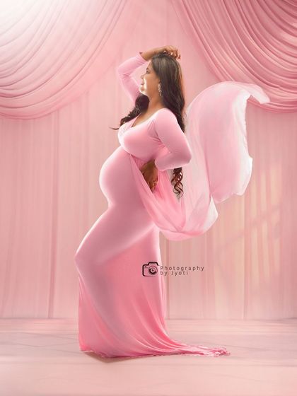 A graceful and artistic pose in a pink gown against a draped pink backdrop. The flowing fabric creates a sense of movement and elegance.