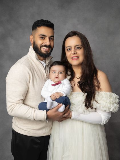 A classic portrait of a beautiful young family. The parents hold their baby, all looking poised and happy for their first family photoshoot.