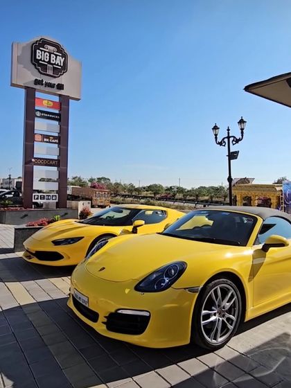 A pair of stunning yellow sports cars, a Porsche Boxster and a Ferrari, brightening up our parking area under a clear blue sky.