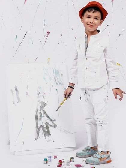 A full-body shot of our little artist standing proudly next to his canvas. The all-white outfit makes the paint splatters stand out beautifully.
