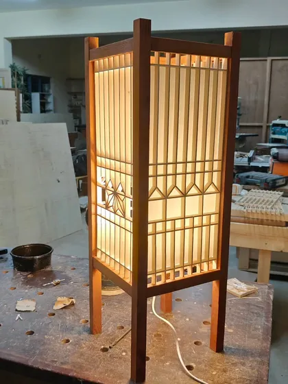 A finished Kumiko lamp, lit up to show the beautiful interplay of light and shadow through the wooden lattice. This one features the classic Asanoha pattern, made from delicate strips of white ash wood.