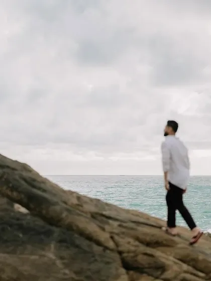 A solo shot of Harman walking along the rocky shoreline, creating a thoughtful and cinematic portrait.