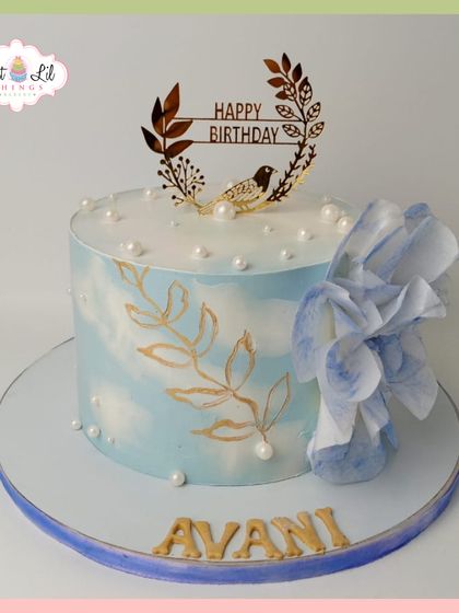 A serene and elegant birthday cake for Avani. The light blue watercolor effect is complemented by hand-painted gold leaves and a large, delicate wafer paper flower.