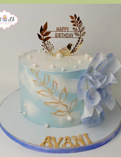 A serene and elegant birthday cake for Avani. The light blue watercolor effect is complemented by hand-painted gold leaves and a large, delicate wafer paper flower.