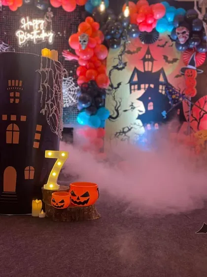 A spooky and fun Halloween-themed birthday party. The setup includes a haunted house backdrop, character cutouts like ghosts, and dry ice fog for a dramatic effect.