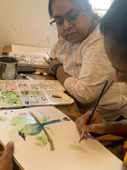 An instructor helps a student with her watercolor bird painting. This hands-on assistance ensures that students learn techniques correctly and feel supported throughout the process.