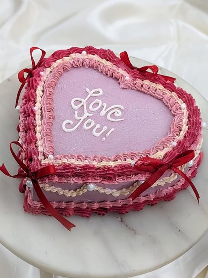 A still shot of our vintage heart cake, showcasing the layered piping work in shades of pink and red, adorned with pearls and ribbons.