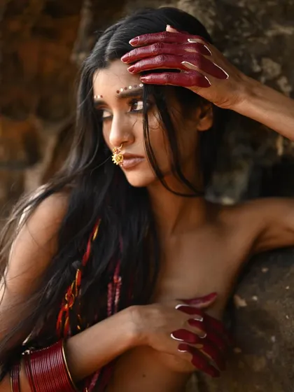 A creative editorial look featuring long, flowing hair with red thread accents and a dramatic reverse cat-eye. The makeup includes intricate dot work along the browline for a tribal-inspired aesthetic.