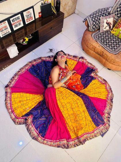 A creative overhead shot of a model lying down, her colorful patchwork Garba lehenga spread out like a flower.