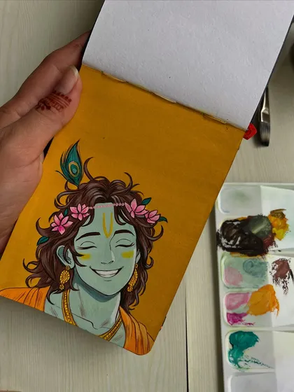 Holding the sketchbook with the Krishna painting, showing the scale of the artwork.