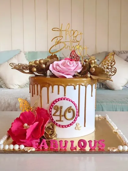 A glamorous "40 & Fabulous" cake with a gold drip, topped with bold pink and gold sugar flowers and butterflies.