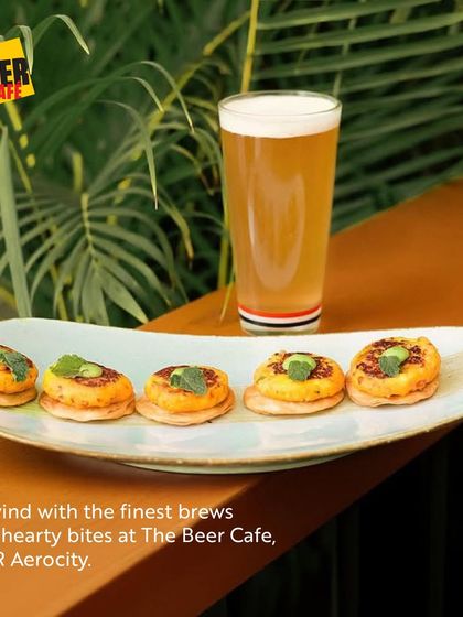 A tall glass of beer next to a plate of hearty bites at The Beer Cafe. It's the perfect setup to unwind with the finest brews and delicious food in a relaxed setting.