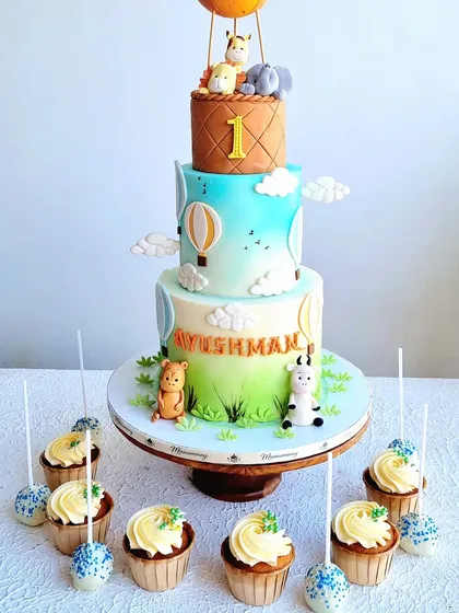 A three-tiered hot air balloon cake with cute fondant animals. The design features a soft color gradient and clouds for a dreamy sky effect.