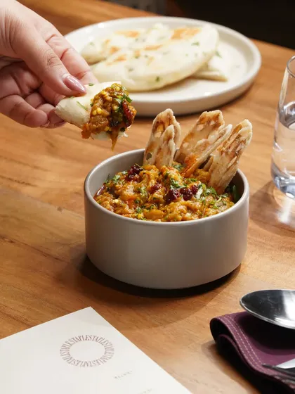 A shot capturing a person enjoying a flavorful bowl of baingan bharta with crispy naan, emphasizing the interactive experience of dining.
