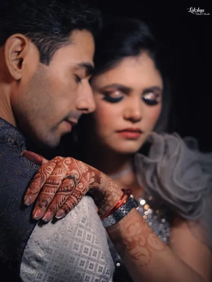 An intimate close-up from an engagement shoot. The focus on the bride's henna-covered hand resting on the groom's shoulder creates a romantic and detailed shot.