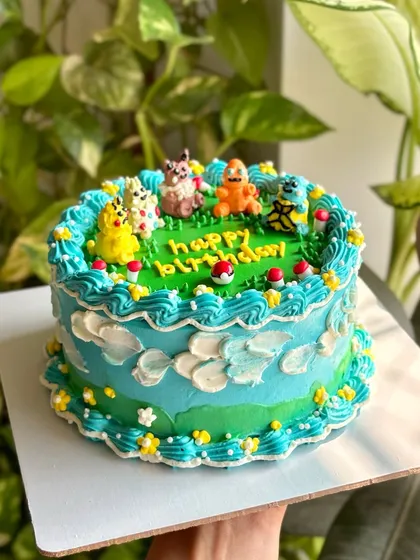 A side view of the Pokémon cake, showing the cloud-like piping and vintage-style border that frames the scene.