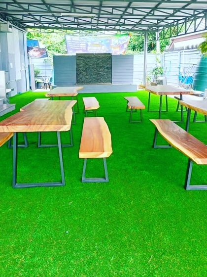 A covered outdoor seating area for a cafe or restaurant, floored entirely with artificial grass. It creates a comfortable, garden-like atmosphere for customers.